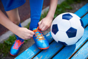 Boy football soccer tying the laces on the boots on bench