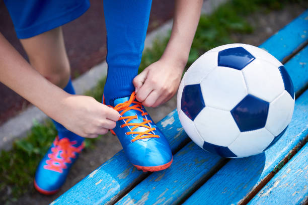 Boy football soccer tying the laces on the boots on bench